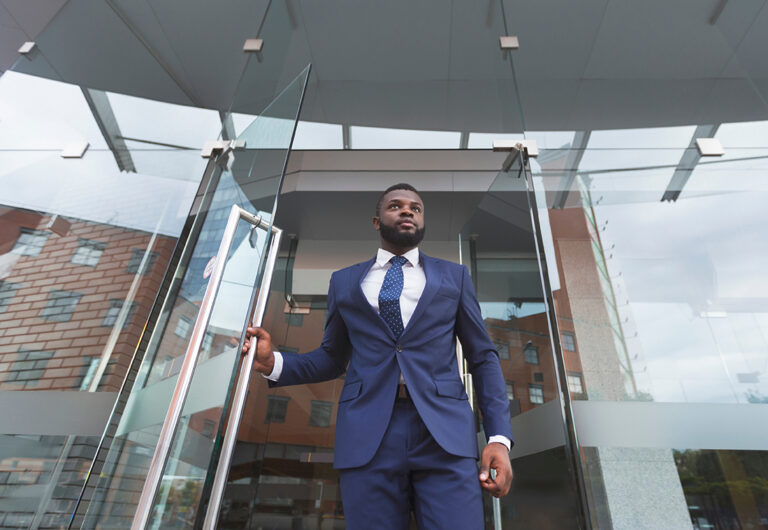 Businessman in a blue suit walking out of a modern office building, representing an employee leaving the workplace after a wrongful termination