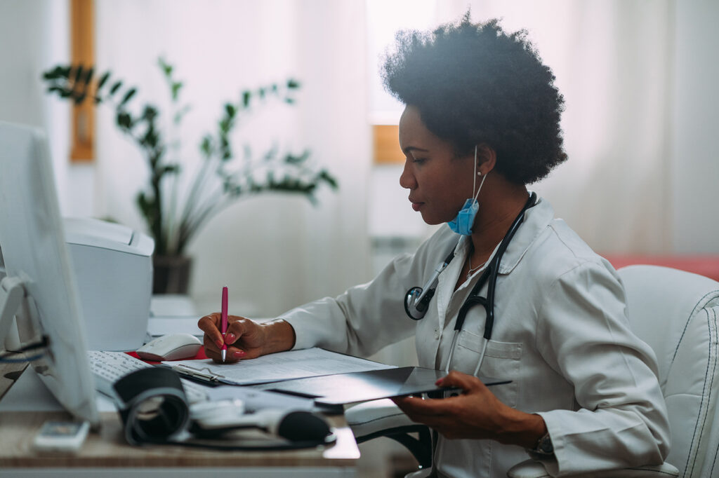 Female doctor in white coat reviewing patient paperwork at her desk, representing the medical industry setting referenced in the blog on signs of workplace harassment