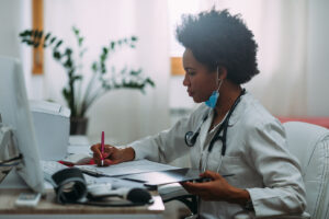 Female doctor in white coat reviewing patient paperwork at her desk, representing the medical industry setting referenced in the blog on signs of workplace harassment