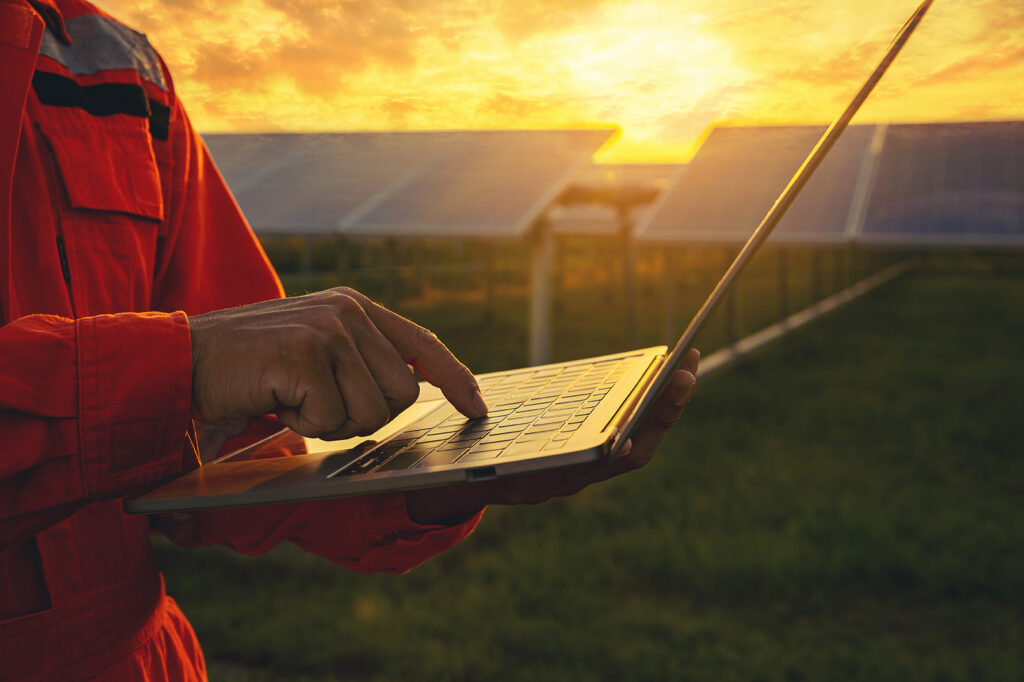 Outdoor worker in Temecula reviewing hours on a laptop near a solar field at sunset