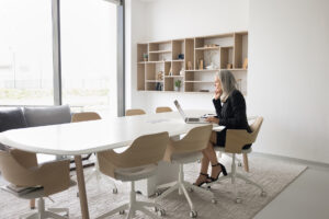 An older businesswoman with gray hair works alone at a laptop in an empty conference room, reflecting the isolation many employees over 40 feel when facing age discrimination at work.