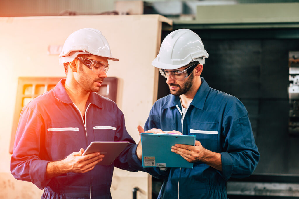 Two factory workers in hard hats and safety glasses reviewing documents together, representing California whistleblower protections for workplace safety concerns