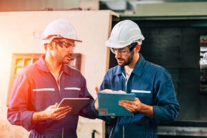 Two factory workers in hard hats and safety glasses reviewing documents together, representing California whistleblower protections for workplace safety concerns