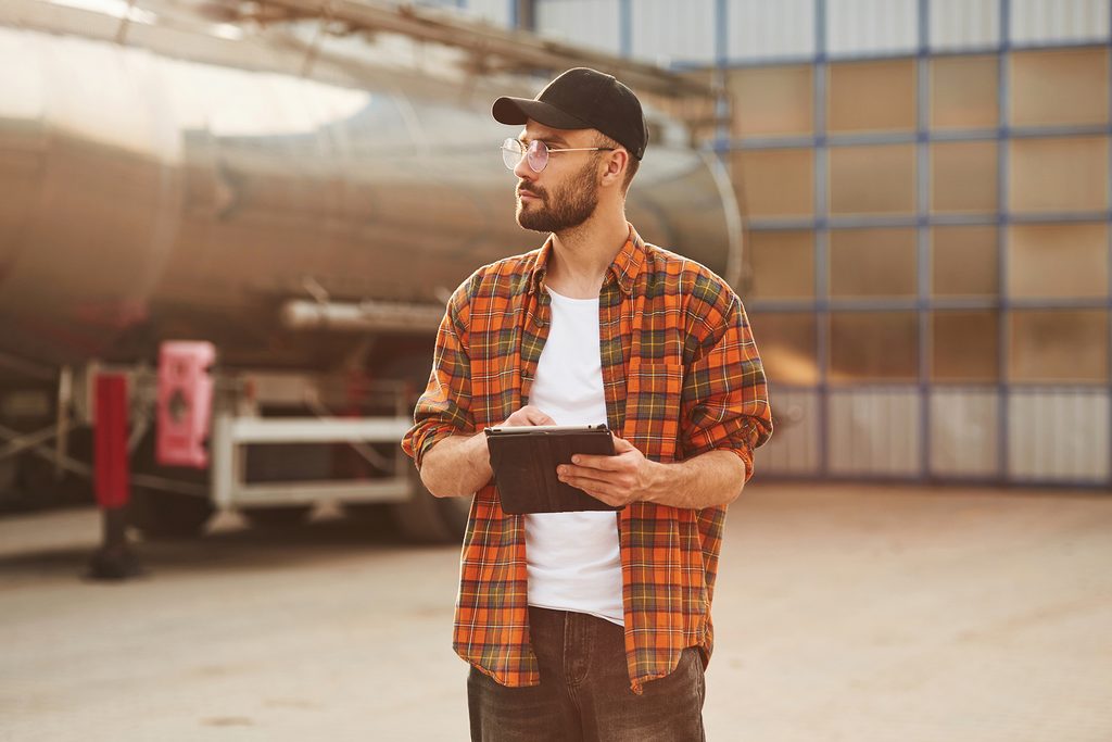 Employee holding a tablet outside a work yard, reviewing his hours for unpaid overtime